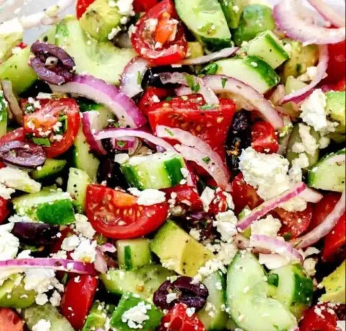 Greek salad with avocado, tomatoes, cucumbers, olives, and feta cheese.