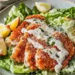 Delicious Chicken Caesar Salad with crispy schnitzel and yoghurt dressing served on a plate.