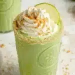 Creamy coconut key lime pie smoothie in a glass with lime slices and a straw